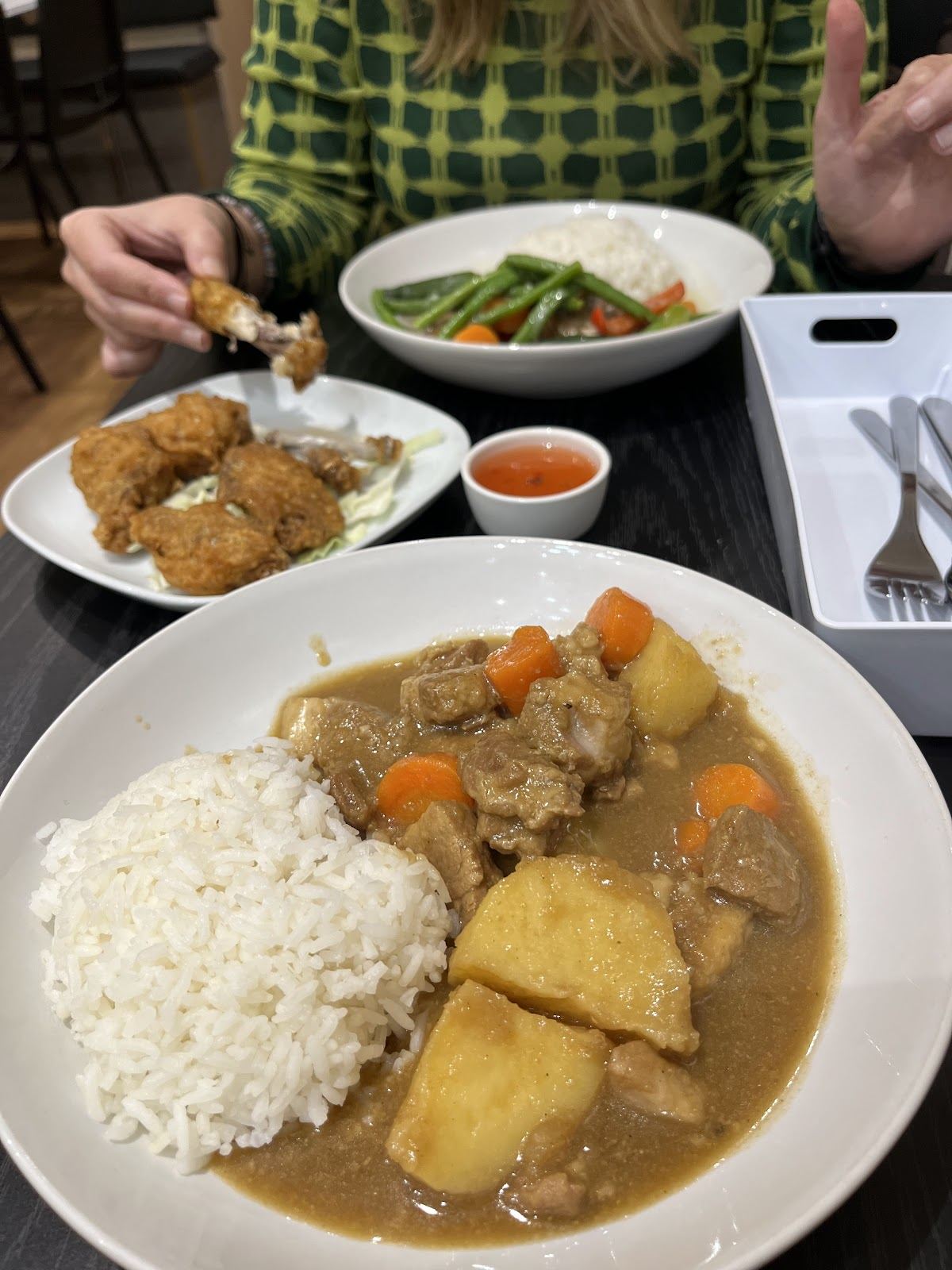 Curry with potato and carrot beside a mound of rice, with fried chicken and a green bean stir-fry behind