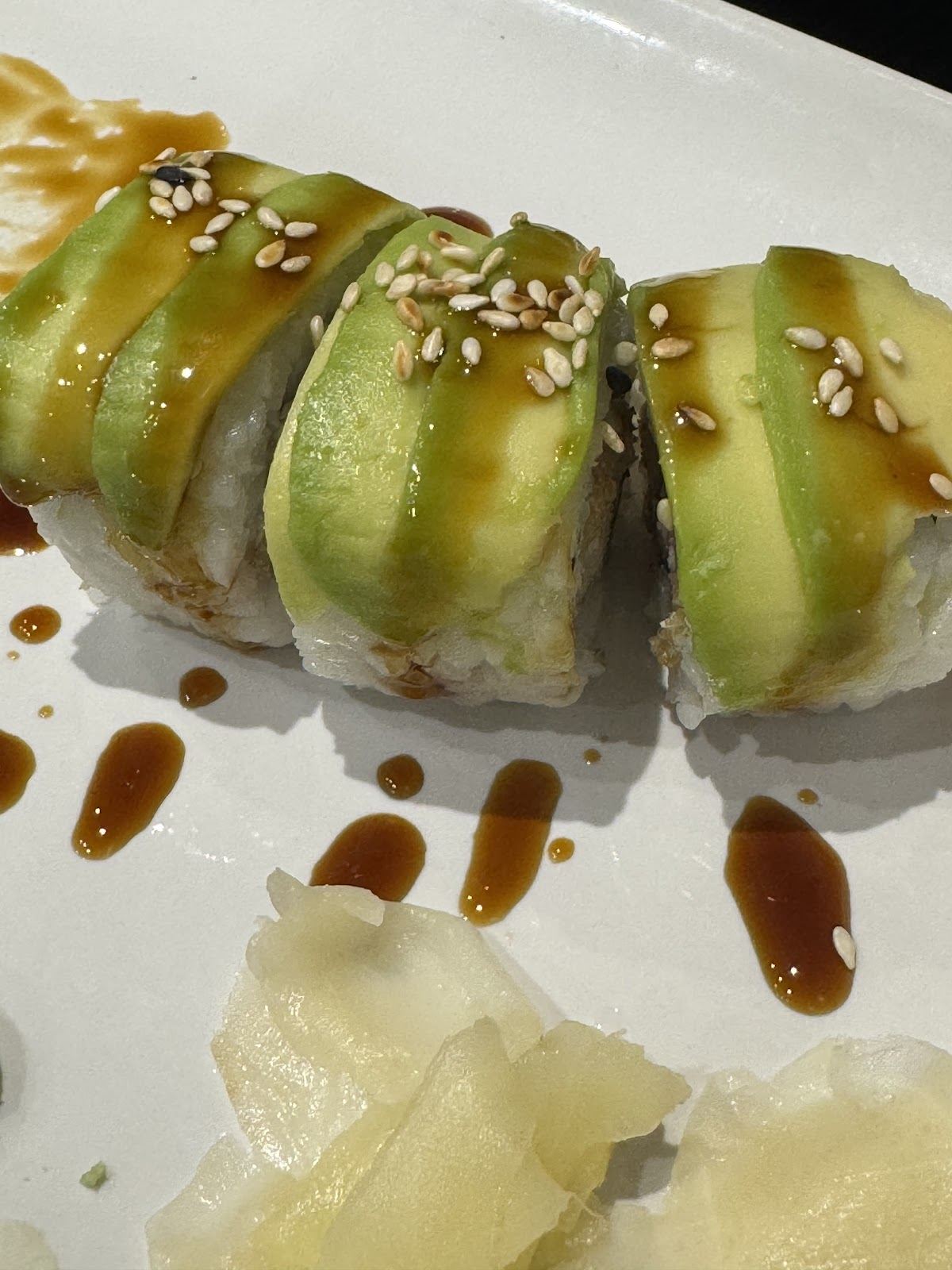 Sushi roll topped with avocado, sesame and sweet soy