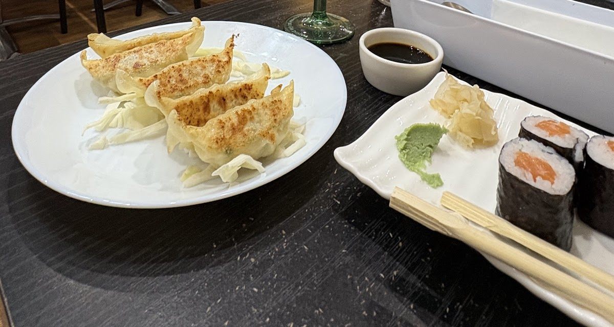 Pan-fried gyoza on shredded cabbage next to salmon maki, ginger and wasabi